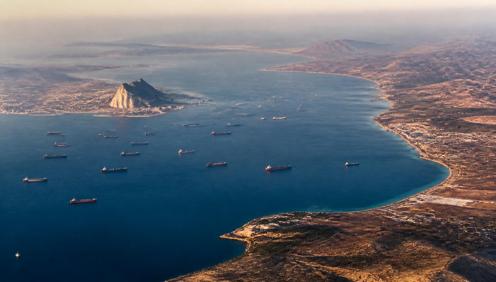 Vista aérea del Estrecho de Gibraltar al atardecer, con decenas de buques mercantes fondeados y el Peñón visible en la orilla europea.